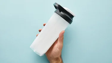 Best protein shaker - cropped view of man holding sports bottle with protein shake on blue